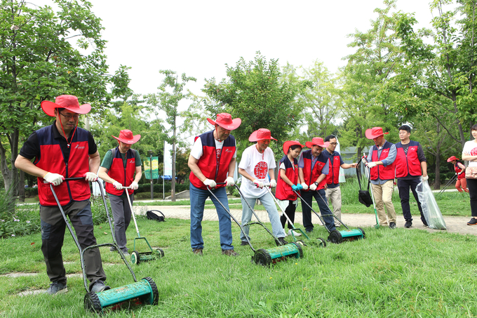 지난 15일 서울숲공원 자원봉사에 참여한 김태영 은행연합회장과 사원은행 임직원 등이 수동식 잔디깎기를 이용해 잔디 관리를 하고 있다. <사진=은행연합회>