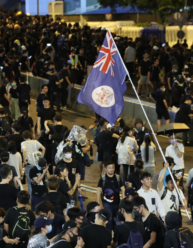 18일 밤 홍콩 정부청사 앞에서 민간인권전선 주도로 열린 송환법 반대, 경찰 강경 진압 규탄 집회에 참가했던 시위대가 홍콩이 1997년 중국에 반환되기 전 사용됐던 영국령 홍콩 깃발을 들고 이동하고 있다 <사진=연합뉴스>