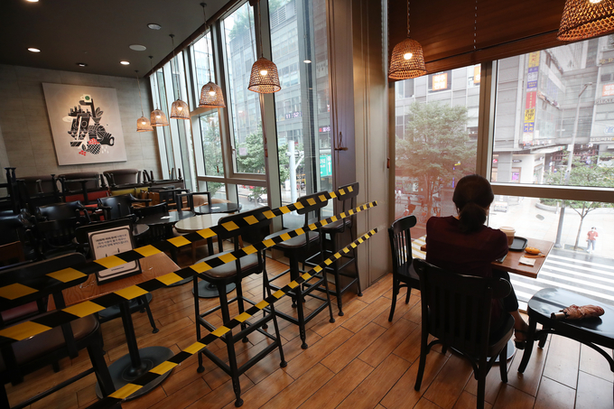 사회적 거리두기 2단계가 조치 중인 지난 21일 서울의 한 카페의 이용객 곁에 사용하지 않는 테이블과 의자가 쌓여있는 모습. <사진=연합뉴스>