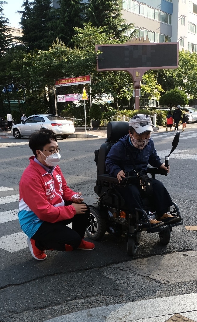 박새롬 후보가 휠체어 장애인의 횡단보도 건널목을 지키며 인사하고 있다. (사진제공=박새롬 후보 선거사무소)