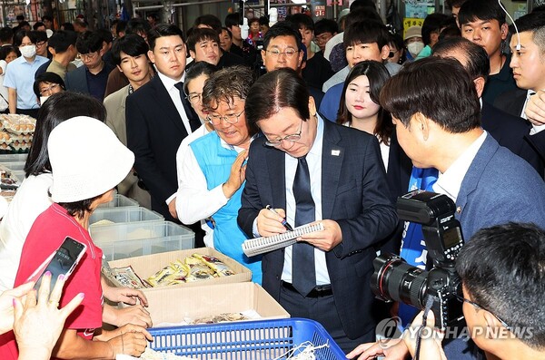23일 낮 전남 영광군 영광터미널시장에서 이재명 더불어민주당 대표가 상인들에게 전달할 사인을 하고 있다. [사진=연합뉴스]